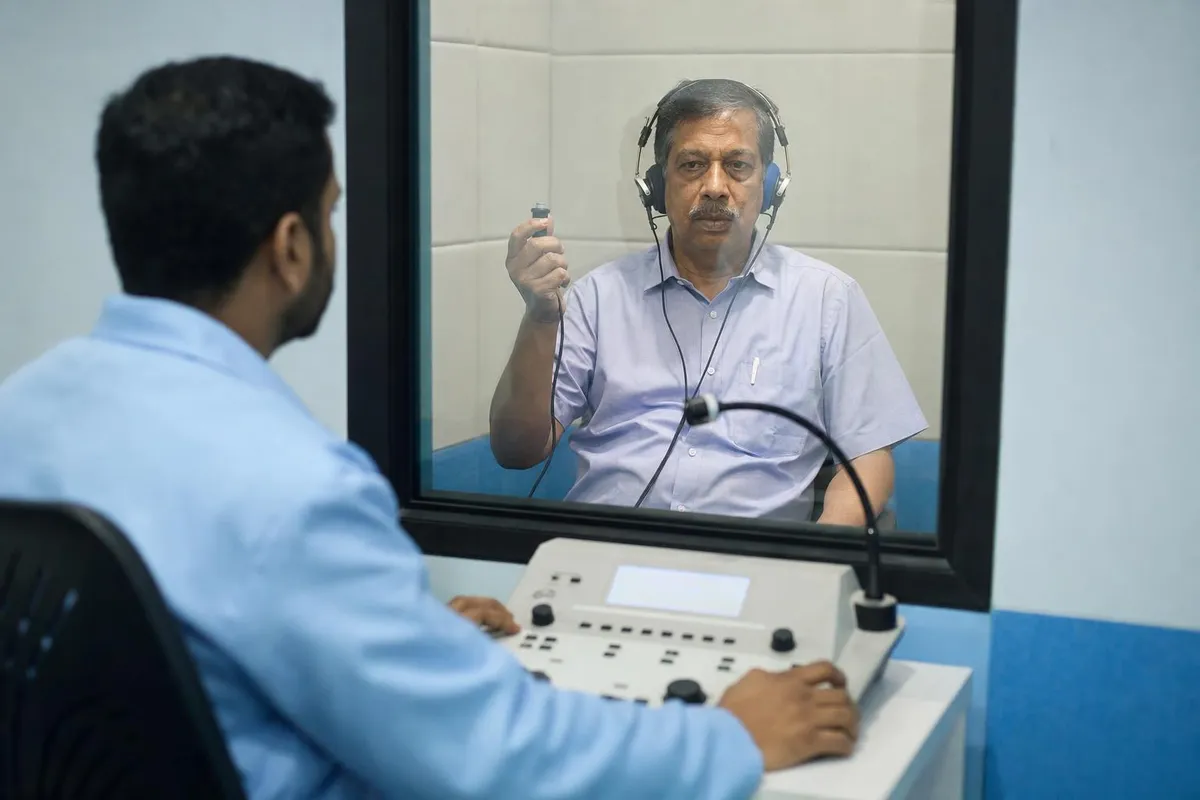Audiologist conducting a pure-tone hearing test with a patient in the sound booth